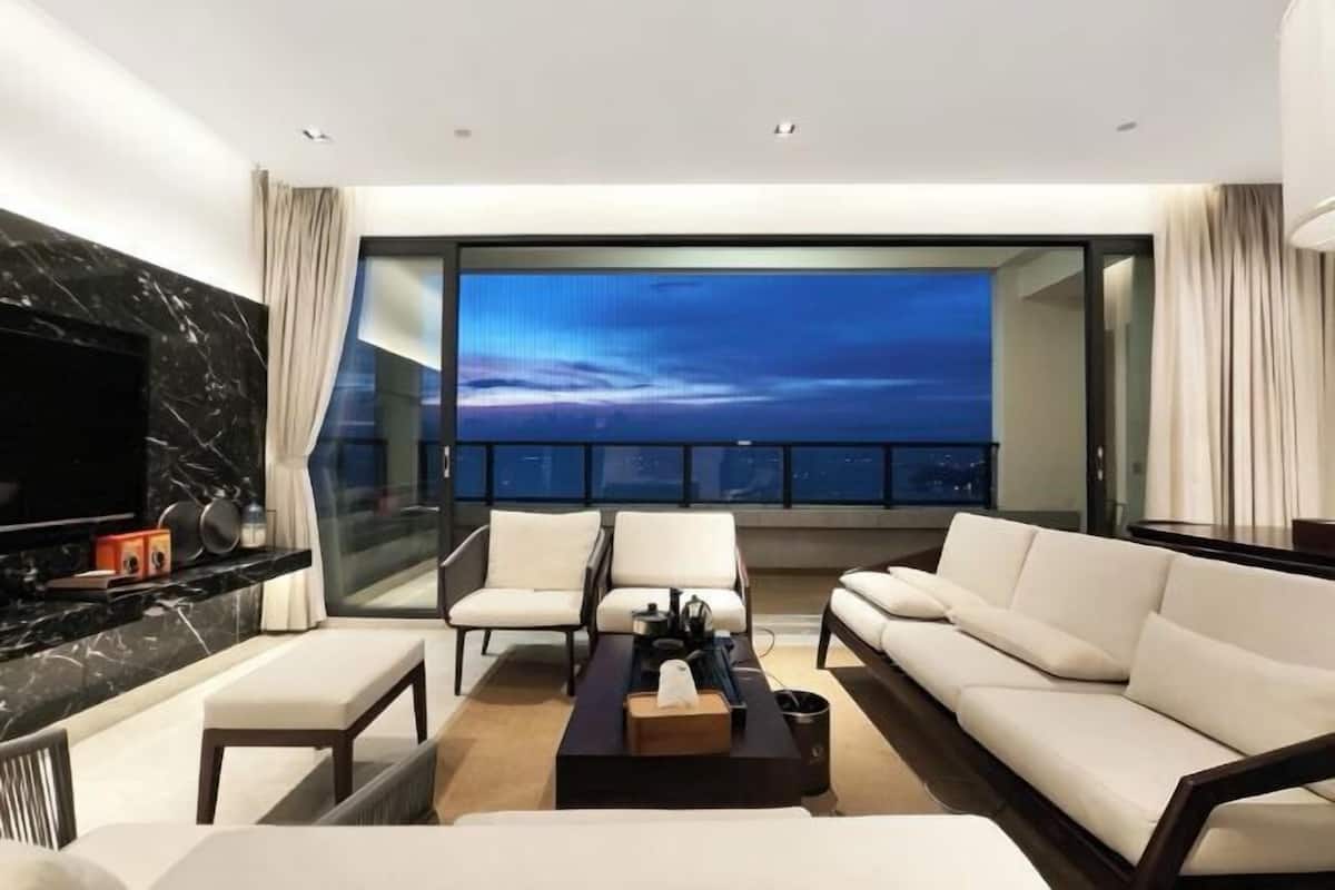 A modern living room with a large TV, comfortable seating, and a balcony with a city view.