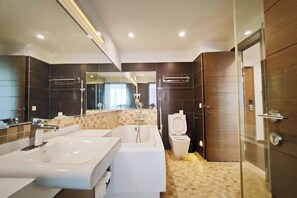 Une salle de bain moderne avec un grand miroir, deux lavabos, une baignoire et des toilettes.