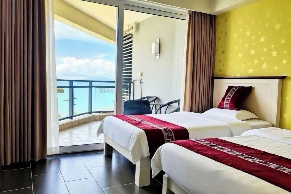 A hotel room with two beds, a balcony with a view, and a yellow wall with star patterns.