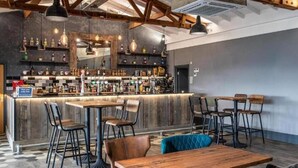 Zona de bar con mostrador, taburetes y luces colgantes.