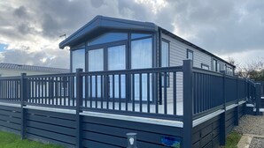 Una casa móvil moderna de un piso, con fachada azul oscuro, ventanas amplias y porche cubierto.