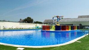 Una piscina con tobogán y una pequeña zona de terraza con sillones de descanso.