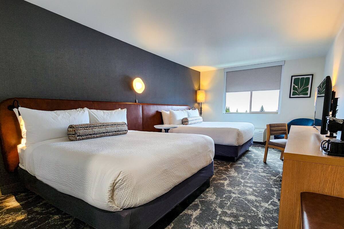 Una habitación de hotel con dos camas, un escritorio, una silla, una lámpara y una ventana.