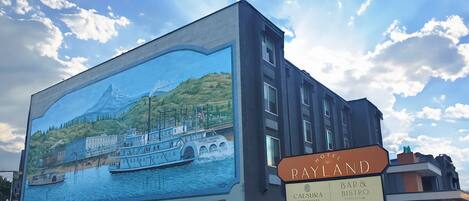 A hotel with a mural of a boat on a lake, a sign for 'Rayland Hotel', and a 'Caesura Coffeehouse'.