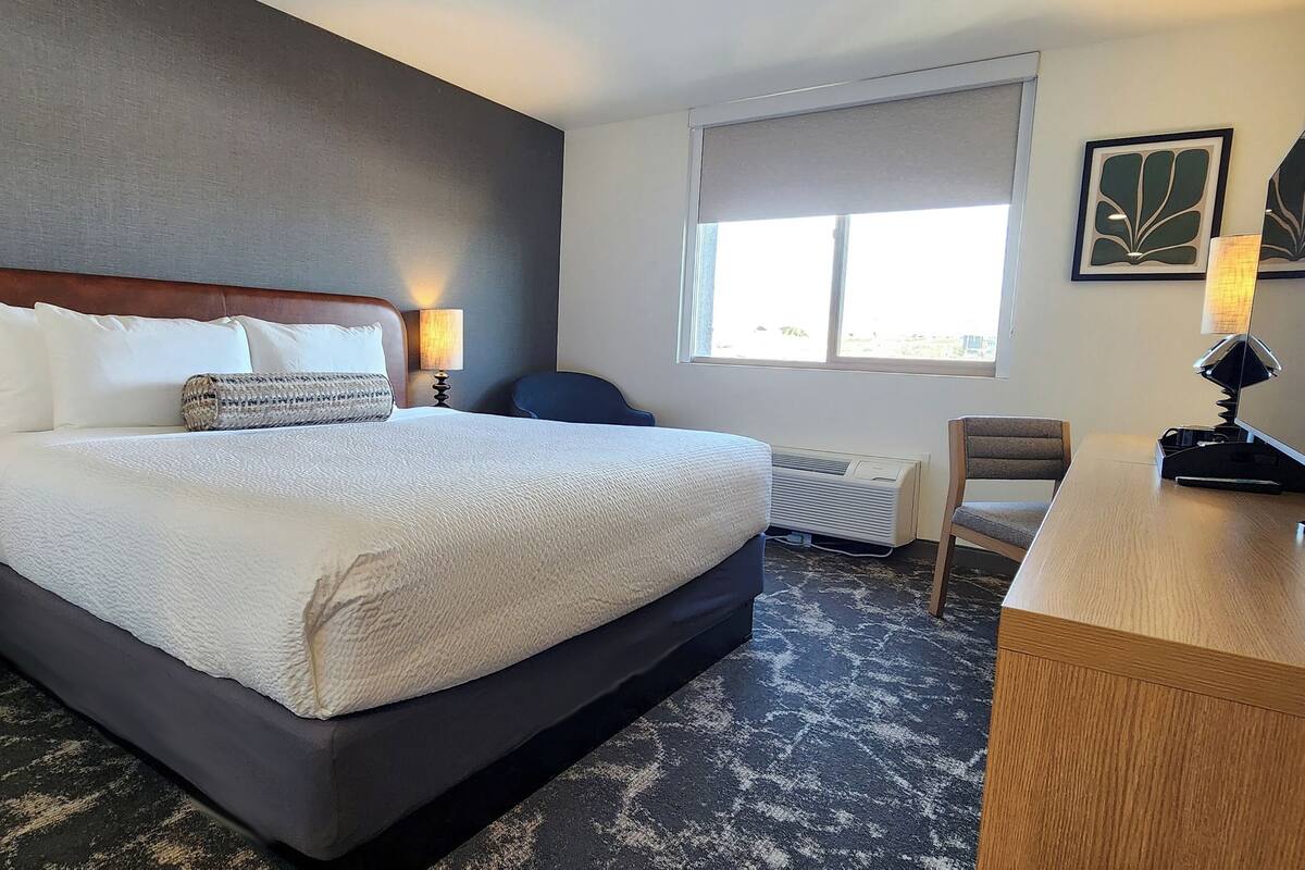 Una habitación de hotel con una cama grande, dos mesitas de noche, un escritorio y una ventana.