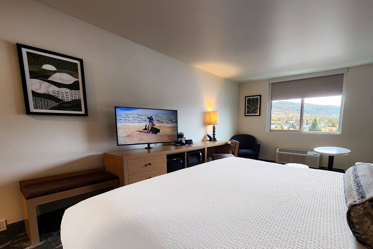 Habitación de hotel con una cama grande, un escritorio con computadora, televisor, lámpara y ventana con vistas a la ciudad.