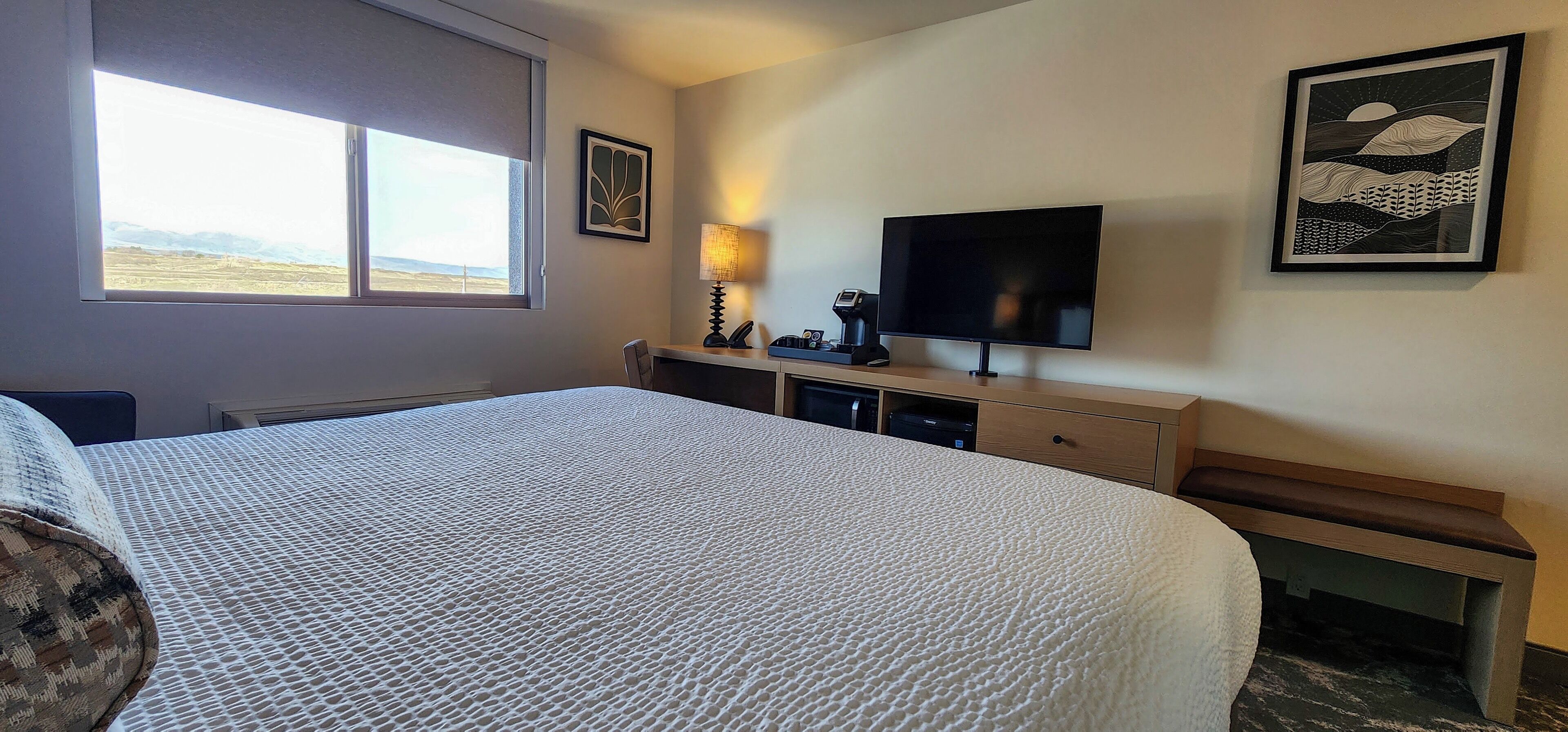 Une chambre d’hôtel avec un grand lit, un bureau avec un ordinateur, une télévision et une fenêtre donnant sur le paysage.