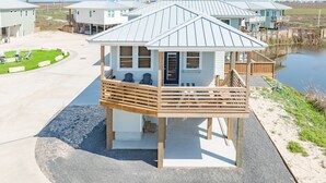 Ein kleines Holzgebäude mit Balkon, vermutlich ein Gästehaus oder ein privates Zimmer, neben einem Gewässer und einem Sandstrand.