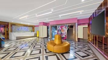 Um lobby moderno com piso de padrão geométrico, uma recepção e uma área de estar amarela e diferenciada.