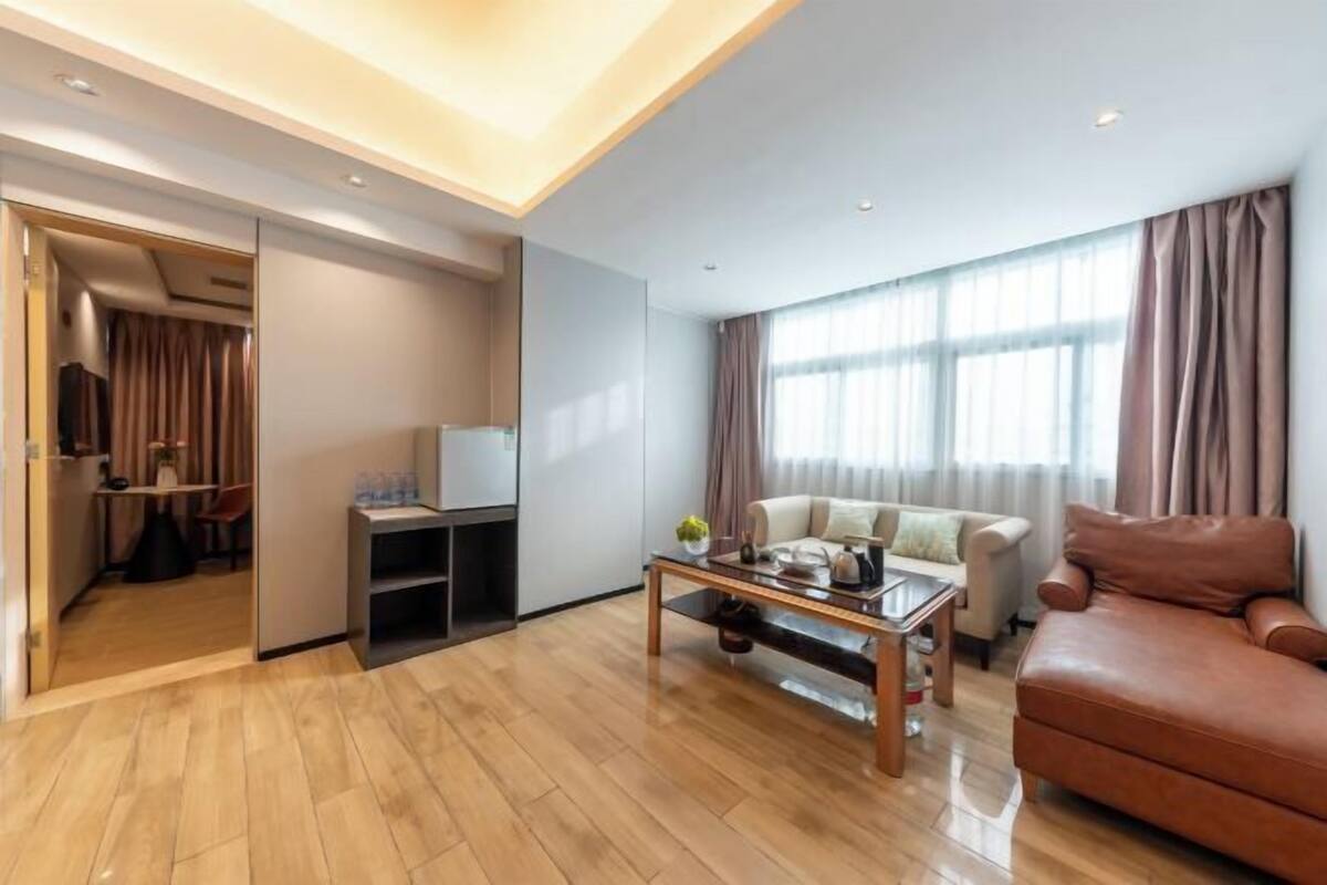 A modern living room with a sofa, a coffee table, and a television. There is a door leading to a kitchen area.