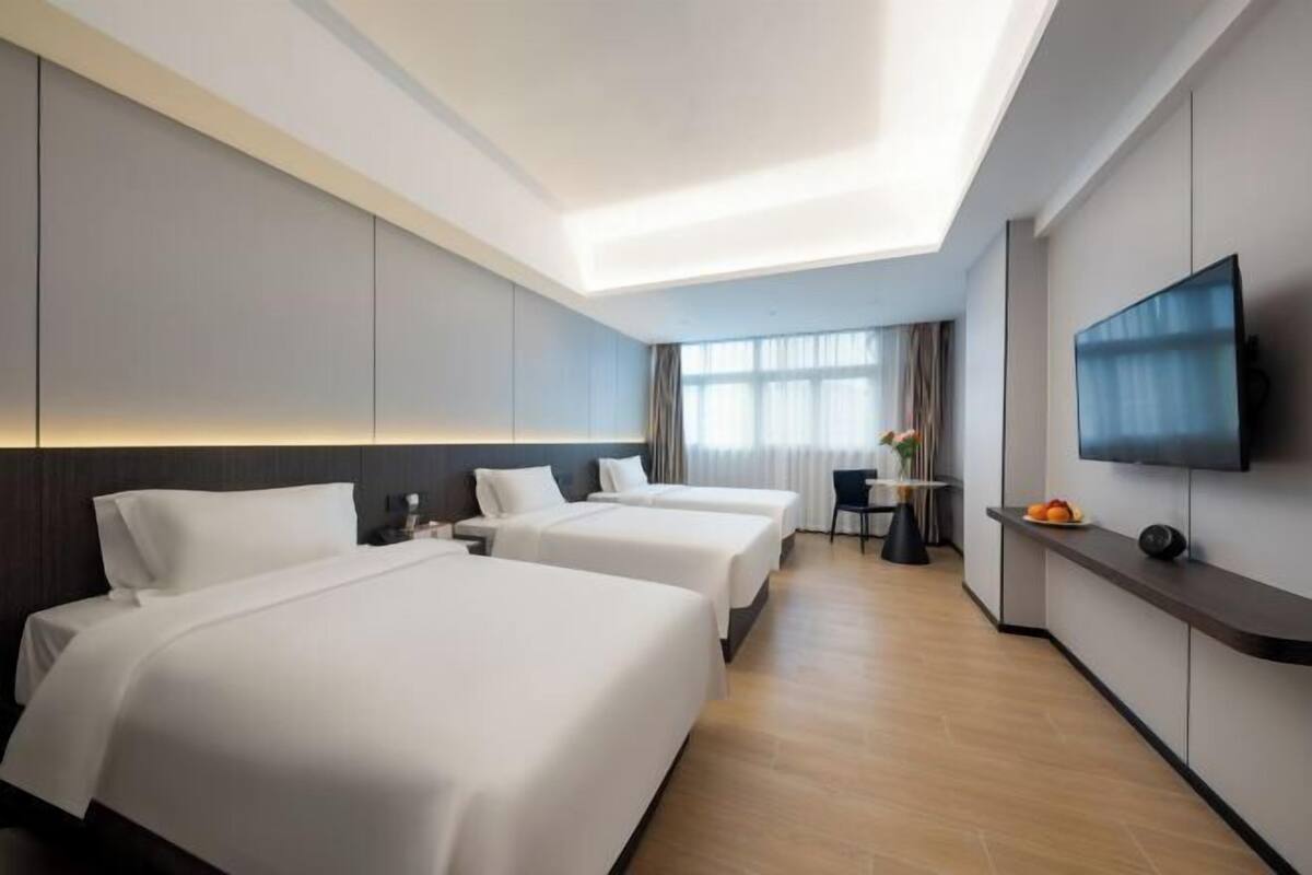 A hotel room with two beds, a TV, a desk, and a window with curtains.