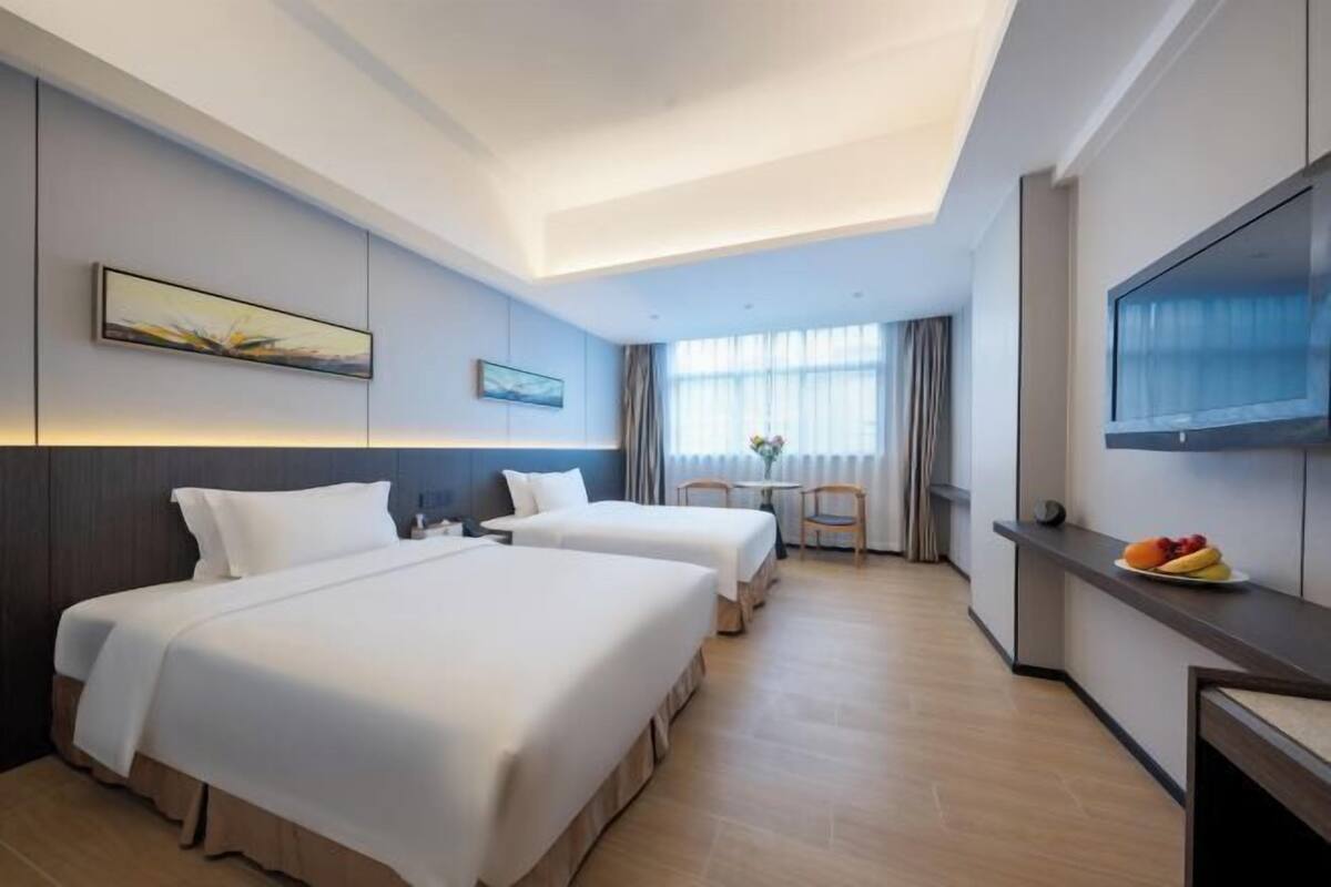 A hotel room with two beds, a desk, a chair, a TV, and a window with curtains.