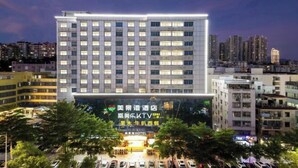 A multi-story hotel with a prominent sign, a parking lot, and surrounding buildings. - Meijingwan Hostel (Shenzhen)