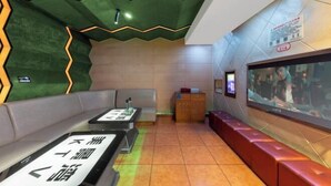 A restaurant with a green and orange patterned ceiling, a large TV screen, and seating areas with tables and benches. - Meijingwan Hostel (Shenzhen)