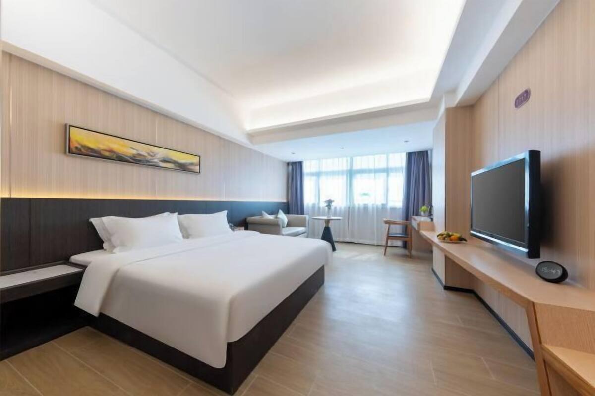A hotel room with a large bed, a TV, a desk, and a window with curtains.