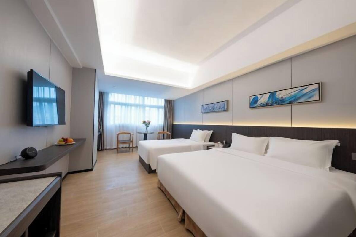 A hotel room with two beds, a desk, a flat-screen TV, and artwork on the walls.