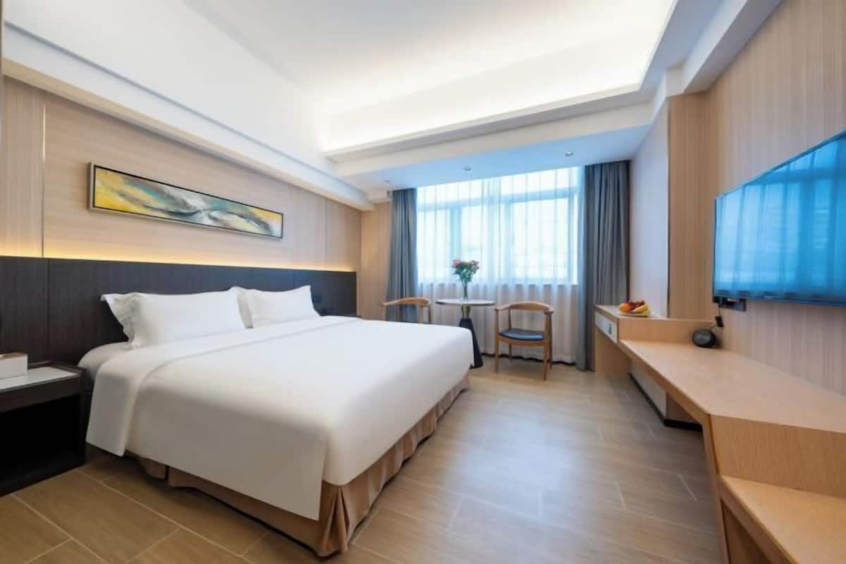 A hotel room with a bed, a desk, a chair, a TV, and a window with curtains.