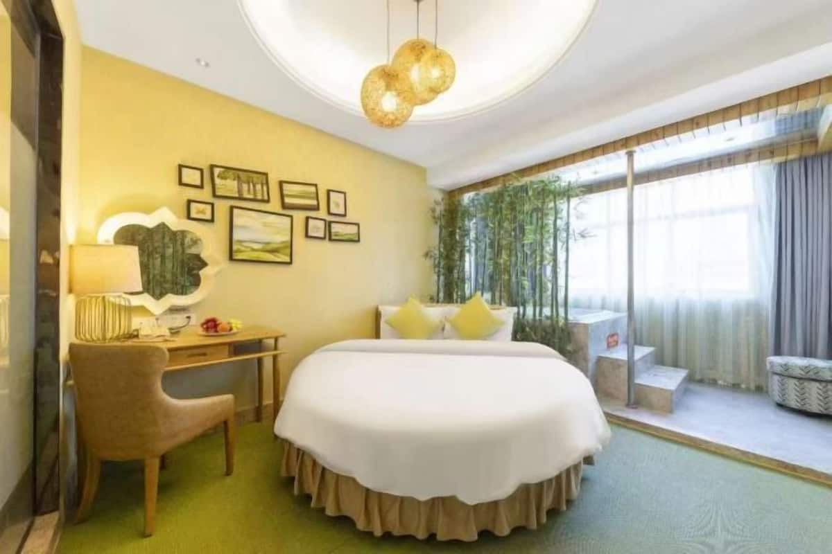 A hotel room with a bed, a desk, a chair, a window with curtains, and wall art.