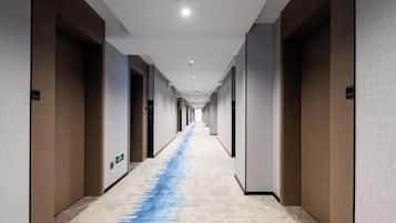 Um corredor de hotel comprido e estreito, com portas de madeira em ambos os lados e um tapete azul ao centro.