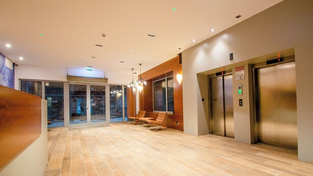 A modern lobby with a wooden reception desk, glass doors leading to a balcony, and two elevators. - Waterlane Island Deluxe 5B by GrandApart (Gdansk)