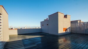 A rooftop terrace with a wooden deck, a small building with a red roof, and a view of the city skyline. - Waterlane Island Deluxe 5B by GrandApart (Gdansk)