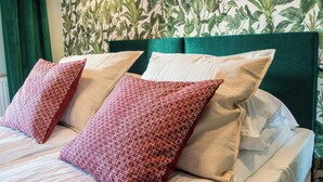 A bed with white and red patterned pillows, a green headboard, and a wall with a leafy wallpaper pattern. - Waterlane Island Deluxe 5B by GrandApart (Gdansk)