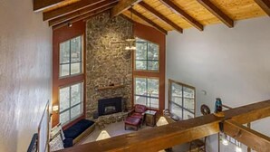 Una sala de estar acogedora con chimenea de piedra, vigas de madera y ventanas amplias.