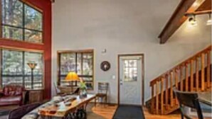 Una habitación amplia con un gran ventanal, una escalera de madera y un comedor con mesa y sillas.