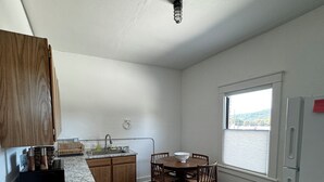 A kitchen with wooden cabinets, a granite countertop, a dining table with chairs, a rug, and a window with blinds. - Charming 2-bedroom apartment in marvelous Chewelah with AC, WiFi (Chewelah)