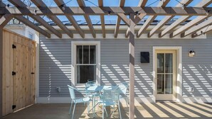 A covered patio with a wooden deck, a table with chairs, and a pergola with string lights. - 3 New Cottages Near Beaches — Sleeps 12 (Burlington)