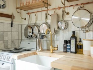 Et køkken med en hvid komfur, rustfrie gryder, en messinghane og diverse køkkenartikler på bordet.