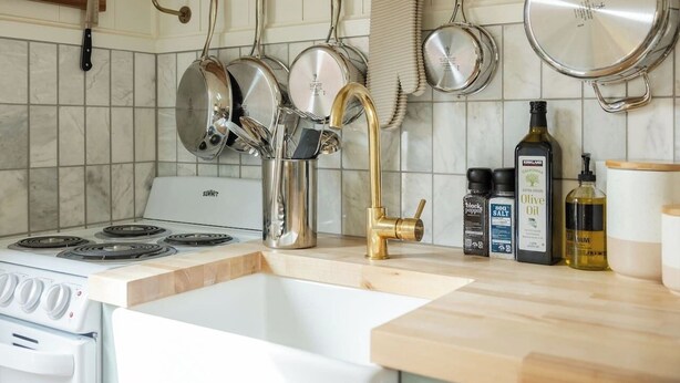 A kitchen with a white stove, stainless steel pots, a brass faucet, and various kitchen items on the counter.