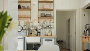 A modern kitchen with wooden shelves, hanging pots, and a white countertop.