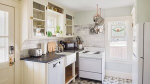 Une cuisine avec des meubles blancs, une cuisinière, un grille-pain et un porte-casseroles suspendu.