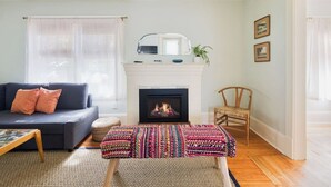Un salon avec une cheminée, un canapé et un banc en osier.