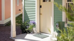 A house with a green exterior, a white door, and a small porch area with a green chair and a potted plant. - Bungalow + 3 Cottages, Whole Estate Sleeps 20 (Burlington)
