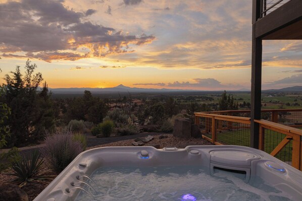 A hot tub with a sunset view, surrounded by a wooden deck and a fence.