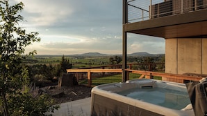 Banyera d'hidromassatge amb vista a un paisatge rural, un pont de fusta i una estructura d'edifici moderna.