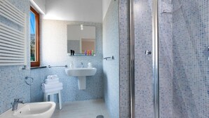 Une salle de bain équipée d’un bidet, d’un lavabo et d’une douche à parois de verre.