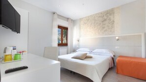 Une chambre à coucher avec un lit, une table de chevet avec une télécommande, une petite table avec des tasses et une fenêtre avec des rideaux.