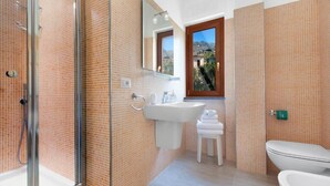 Une salle de bain dotée d’une douche à parois de verre, d’un lavabo blanc, de toilettes et d’une fenêtre donnant sur l’extérieur.