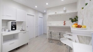 Une cuisine moderne avec des meubles blancs, une machine à café, un évier et un panier de fruits posé sur le plan de travail.