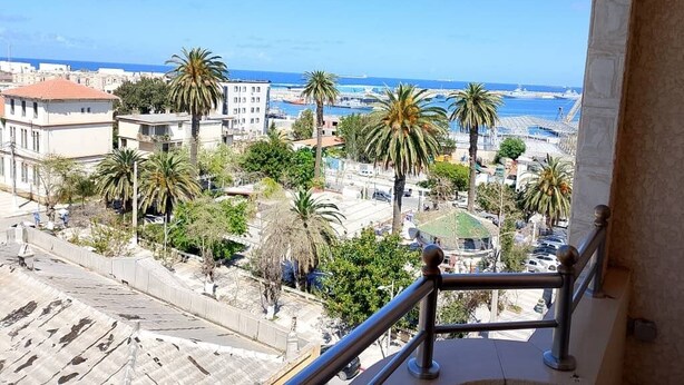 Een balkon met uitzicht op een kuststadsgezicht, met gebouwen en palmbomen.
