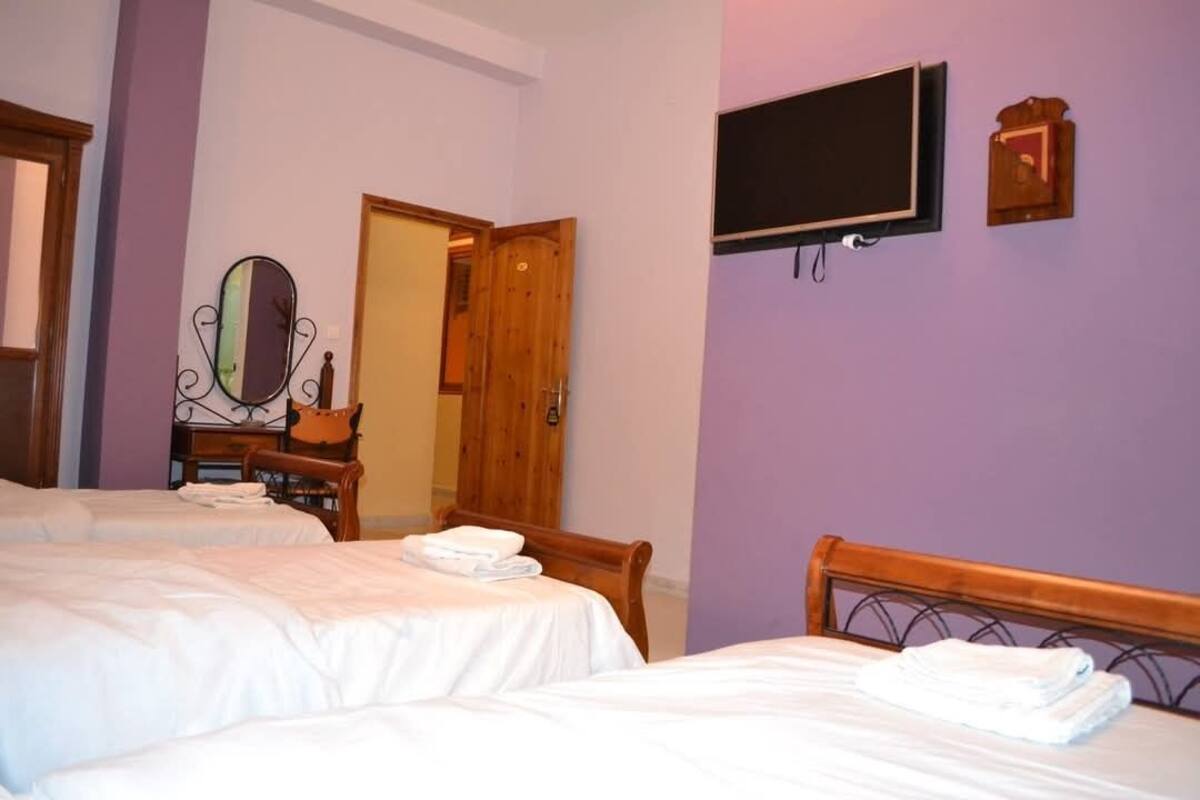 A hotel room with two beds, a television mounted on the wall, a wooden door, and a mirror on the left side.
