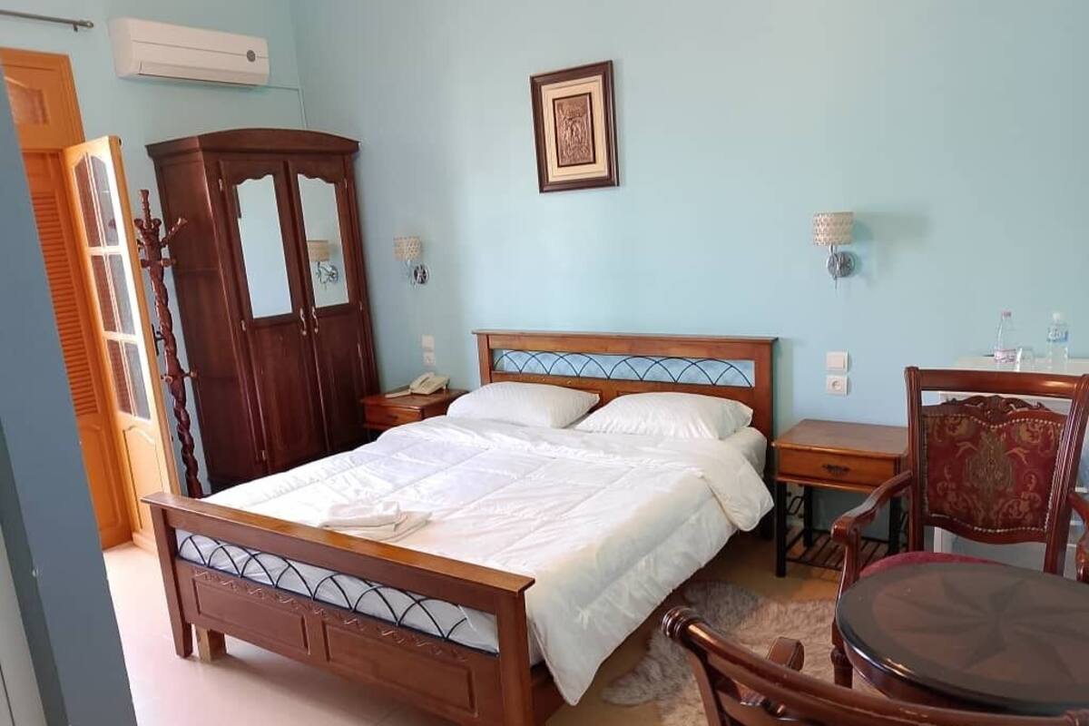 A bedroom with a wooden bed, a wardrobe, a bedside table, a chair, and a small table.