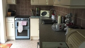 A compact kitchen with a stove, oven, microwave, and a cutting board on the counter. - 3 bed Detached Sound Healing Retreat Bungalow (Cardigan)