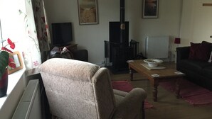 A living room with a sofa, armchair, table, and a fireplace. - 3 bed Detached Sound Healing Retreat Bungalow (Cardigan)