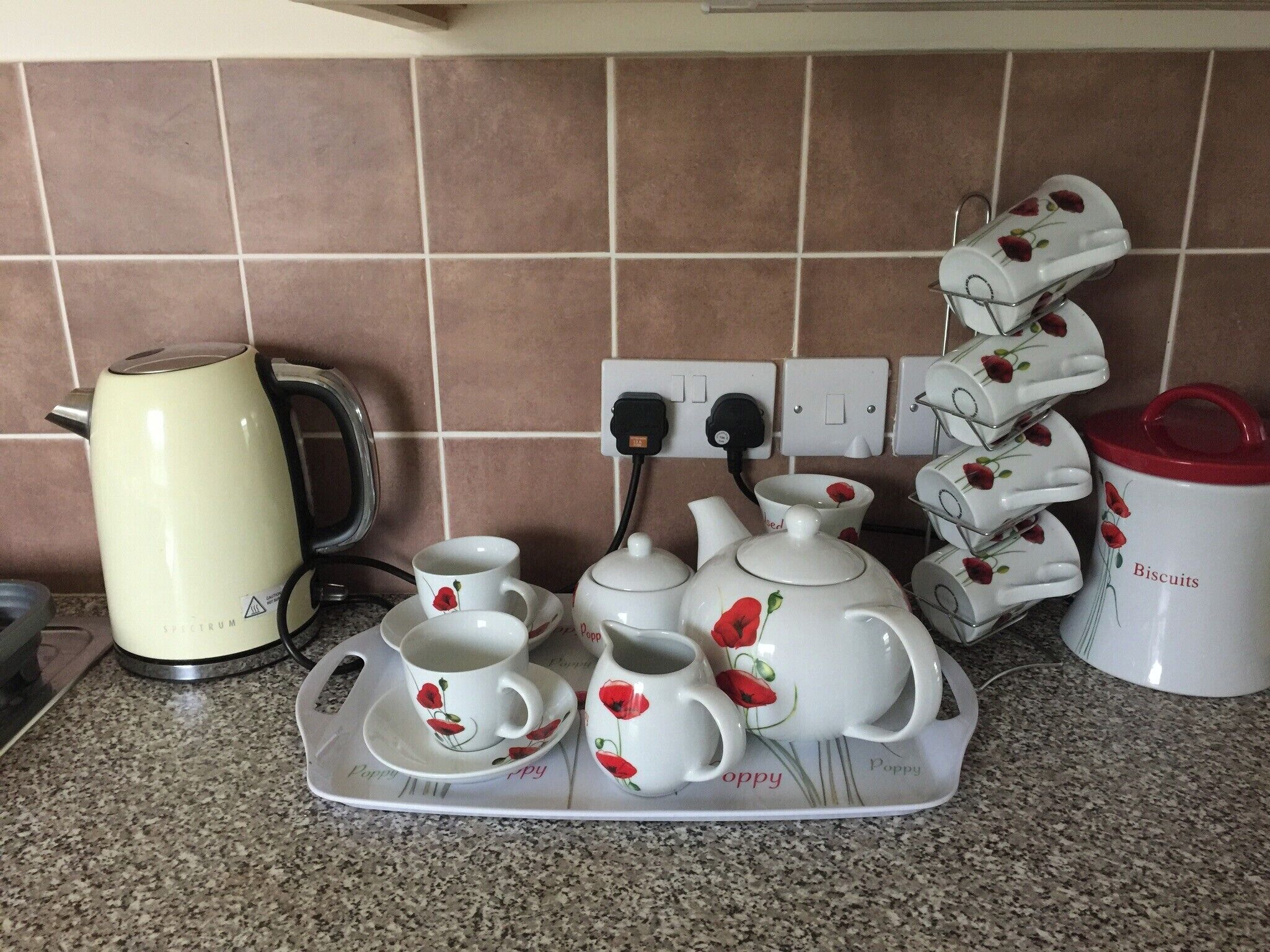 A kitchen with a kettle, teapot, cups, and a tray with a poppy design.
