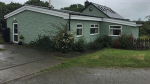 A green stone house with a chimney, a small porch, and a garden. - 3 bed Detached Sound Healing Retreat Bungalow (Cardigan)