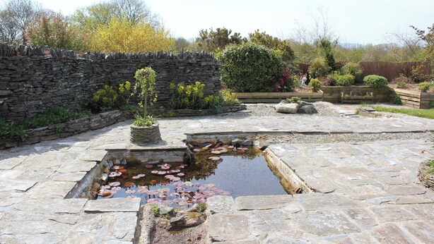 A stone courtyard with a small pond, stone walls, and various plants. - 3 bed Detached Sound Healing Retreat Bungalow (Cardigan)